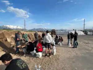 Dedicated community members work together filling sandbags near large sand piles and mountains, ensuring safety with expert care.