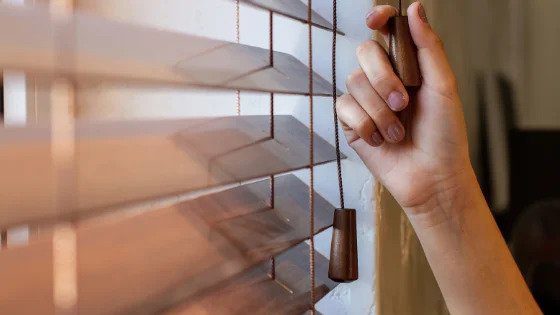 A hand adjusts wooden blinds, letting in natural light—a reminder of Black Diamond Experts’ 24/7 trusted home comfort services.