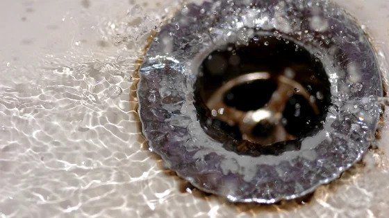 Water swirling around a metal sink drain, a reminder that Black Diamond Experts are here 24/7 for dependable home comfort solutions.