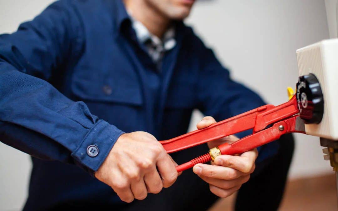 A skilled technician in a blue shirt uses a red wrench on equipment, ensuring safe, expert service for Utah homes—day or night.