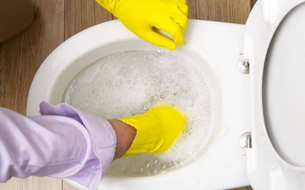 A technician with yellow gloves cleans a soapy toilet, ensuring safe, dependable plumbing support for Utah homes—day or night.