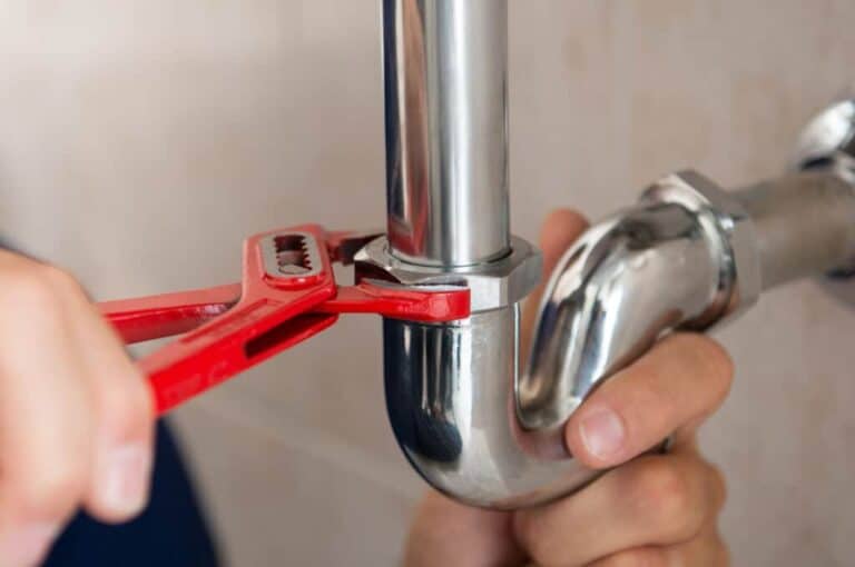 A skilled technician uses a red pipe wrench to secure a metal pipe joint under a sink, ensuring safe, reliable home repairs.
