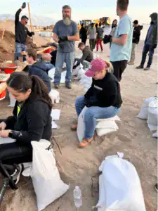 A dedicated team works together outdoors, filling and tying sandbags with care, supported by reliable tools and equipment.